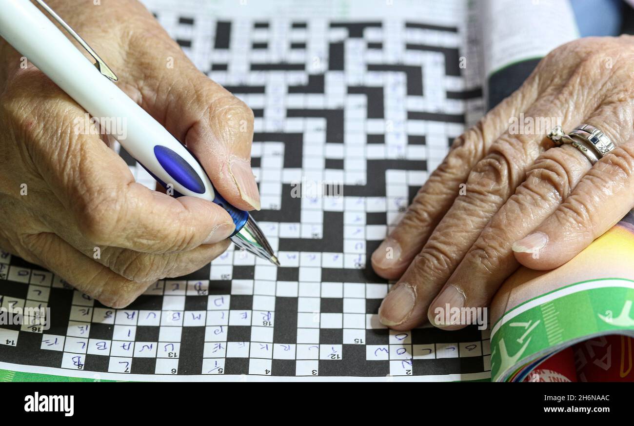 Generisches Bild von weiblichen älteren Händen, die einen Stift benutzen, um ein Kreuzworträtsel zu füllen. Stockfoto