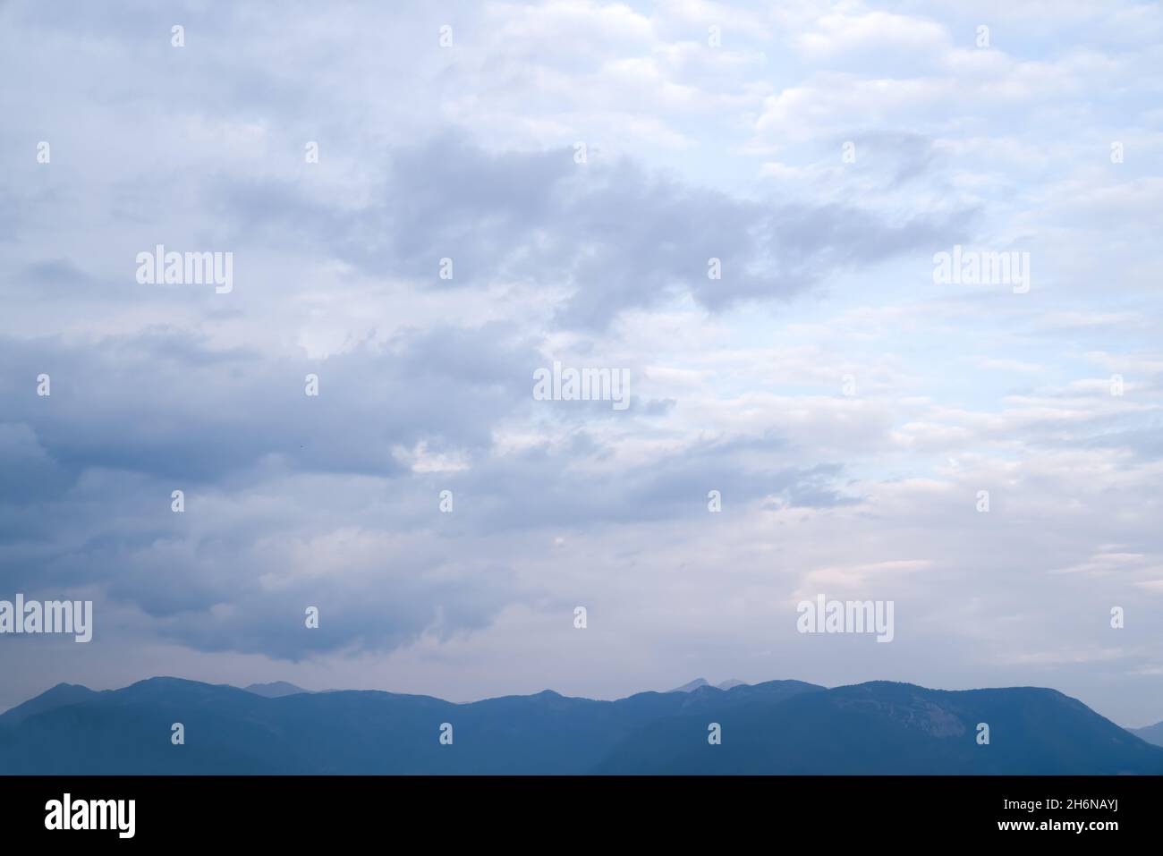 Hintergrund von schönen flauschigen grau-weißen Wolken über Band von Berggipfeln. Natürlicher Hintergrund. Stockfoto