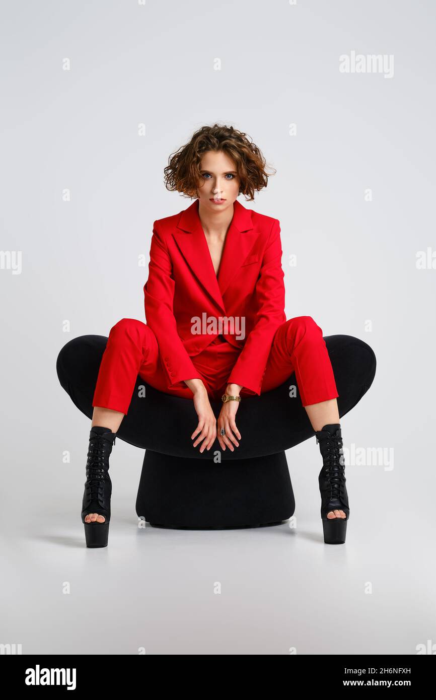 Eine ernsthafte Frau in roten Pantsui- und Polentanzstiefeln sitzt in einem weichen Sessel, der die Beine verteilt Stockfoto