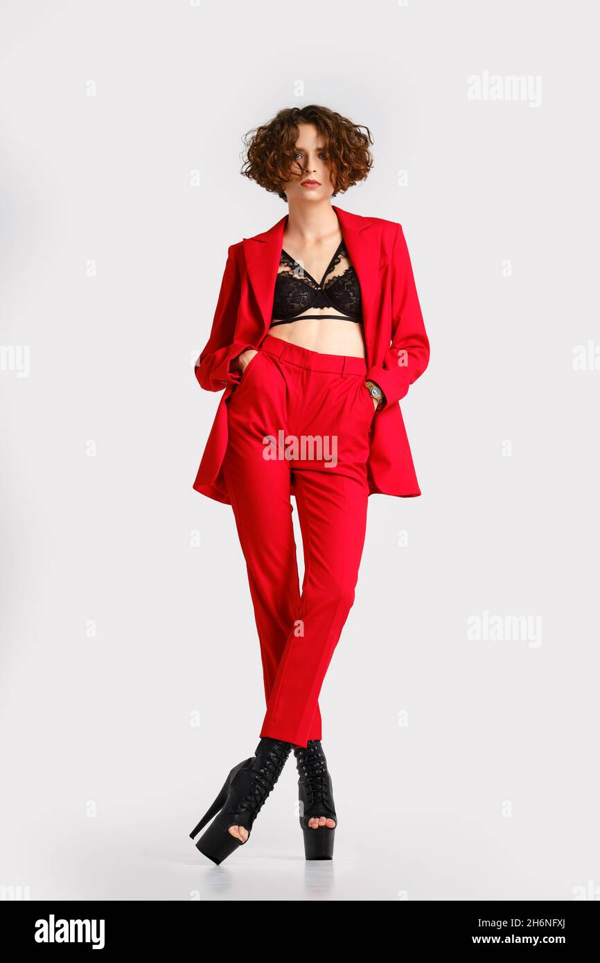 In voller Länge Porträt einer Frau in roten Pantsui und Pole Dance Stiefeln steht mit Händen in Taschen Stockfoto
