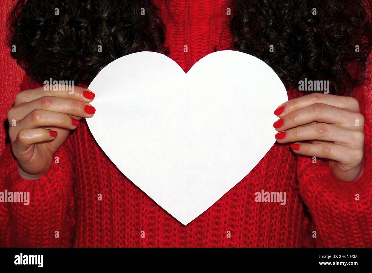 Lockiges Haar Mädchen in roten Pullover hält weißes Herz mit Platz für Text. Valentinstag-Konzept Stockfoto