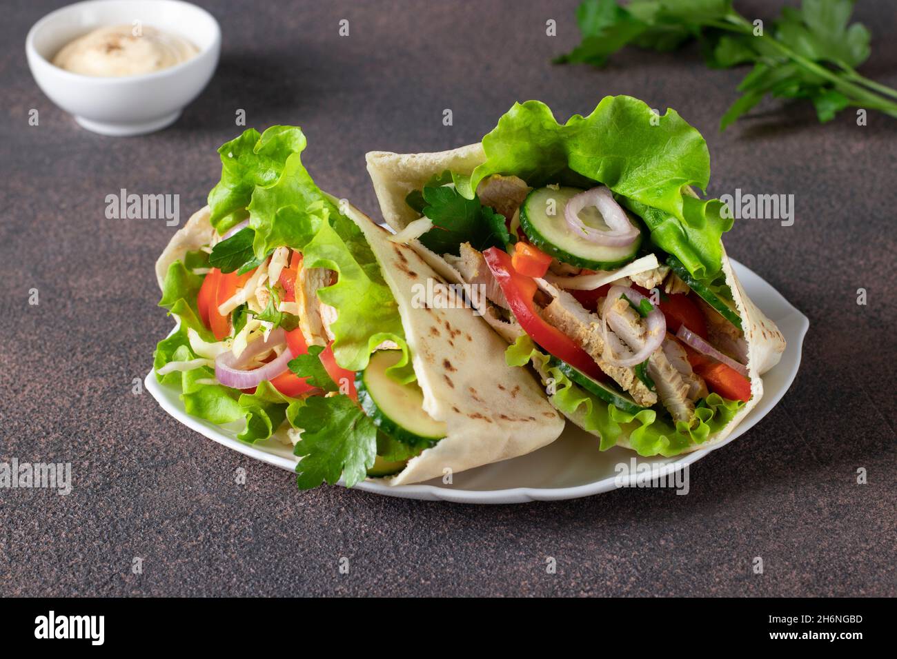 Pita gefüllt mit Huhn, Pfeffer, Gurke und Salat auf weißem Teller. Östliche Küche Stockfoto