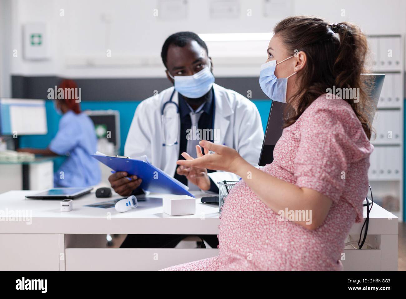 Frau, die ein Kind erwartet und mit einem Arzt über Schwangerschaft und Gesundheitsversorgung diskutiert. Hausarzt, der während einer Coronavirus-Pandemie Schwangeren medizinische Ratschläge gibt Stockfoto