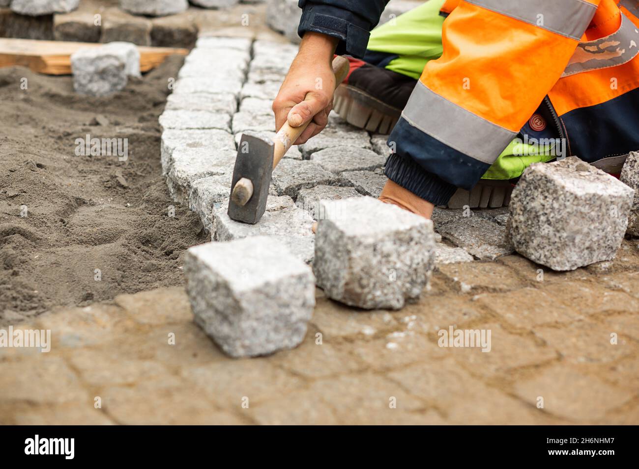 Wartungsarbeiten am Pflaster mit ineinander verschränktem Pflasterstein. Unkenntliche Person mit Baustoffen in der Hand, Betonprodukte, Bauindustr Stockfoto