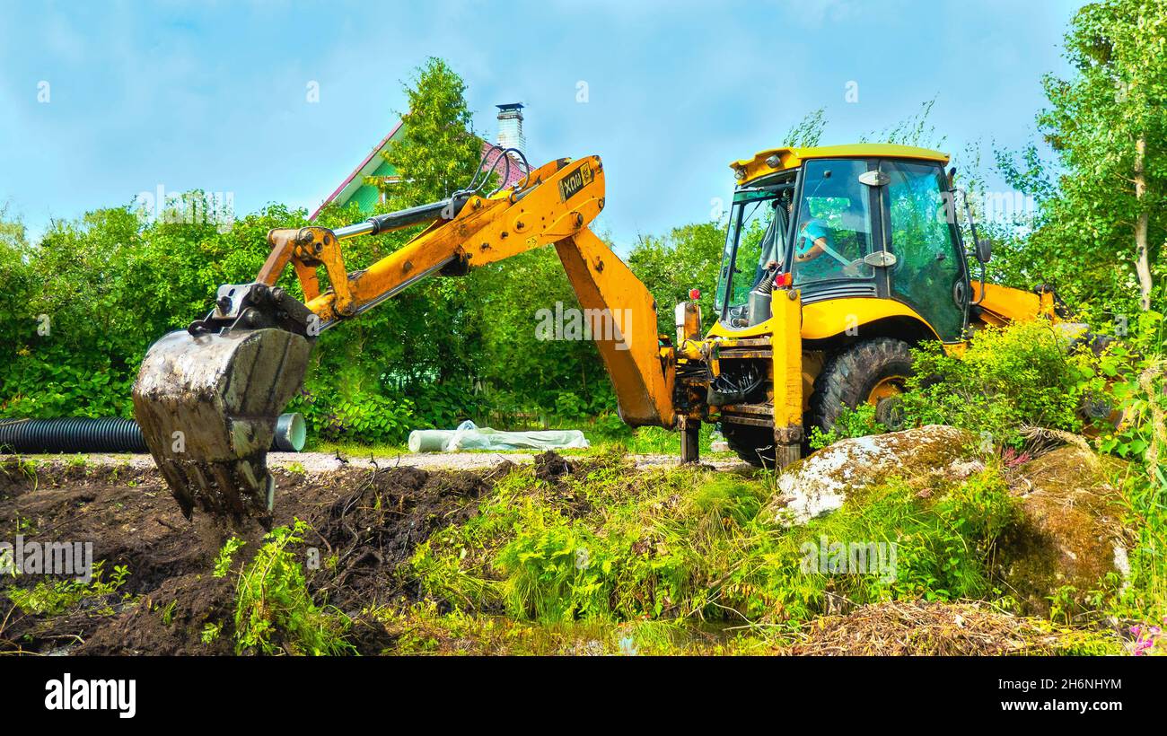 Bagger mit Eimer gräbt oder reinigt einen Graben auf dem Feld unter einem Gras. Hochwertige Fotos Stockfoto