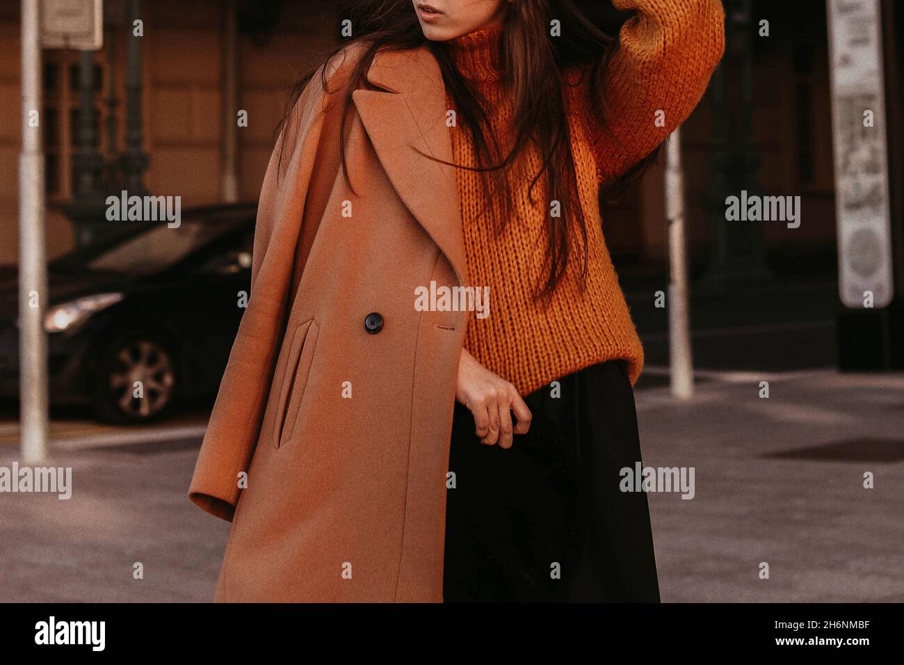 Verkürzte Figur einer jungen Frau in einem braunen, kuscheligen herbstlichen warmen Mantel und Strickpullover. Lässige Street-Fashion. Filmkorneffekt Stockfoto