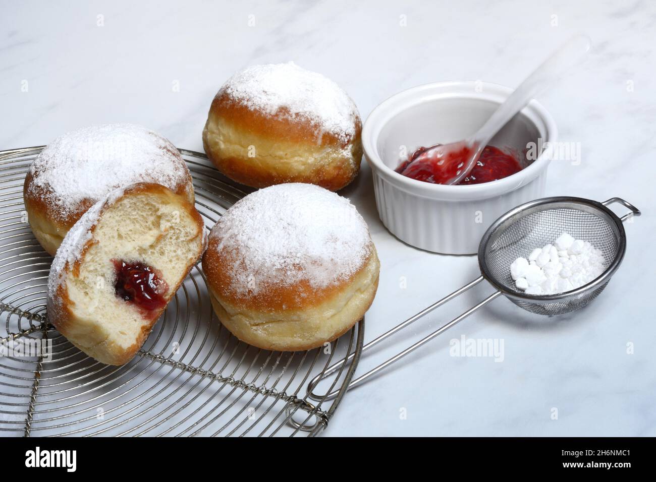 Gefüllte Berliner Pfannkuchen, Schüssel mit Marmelade und Sieb mit Puderzucker Stockfoto