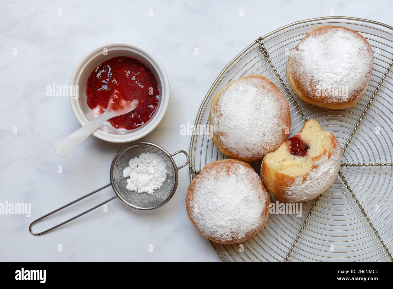 Gefüllte Berliner Pfannkuchen, Schüssel mit Marmelade und Sieb mit Puderzucker Stockfoto