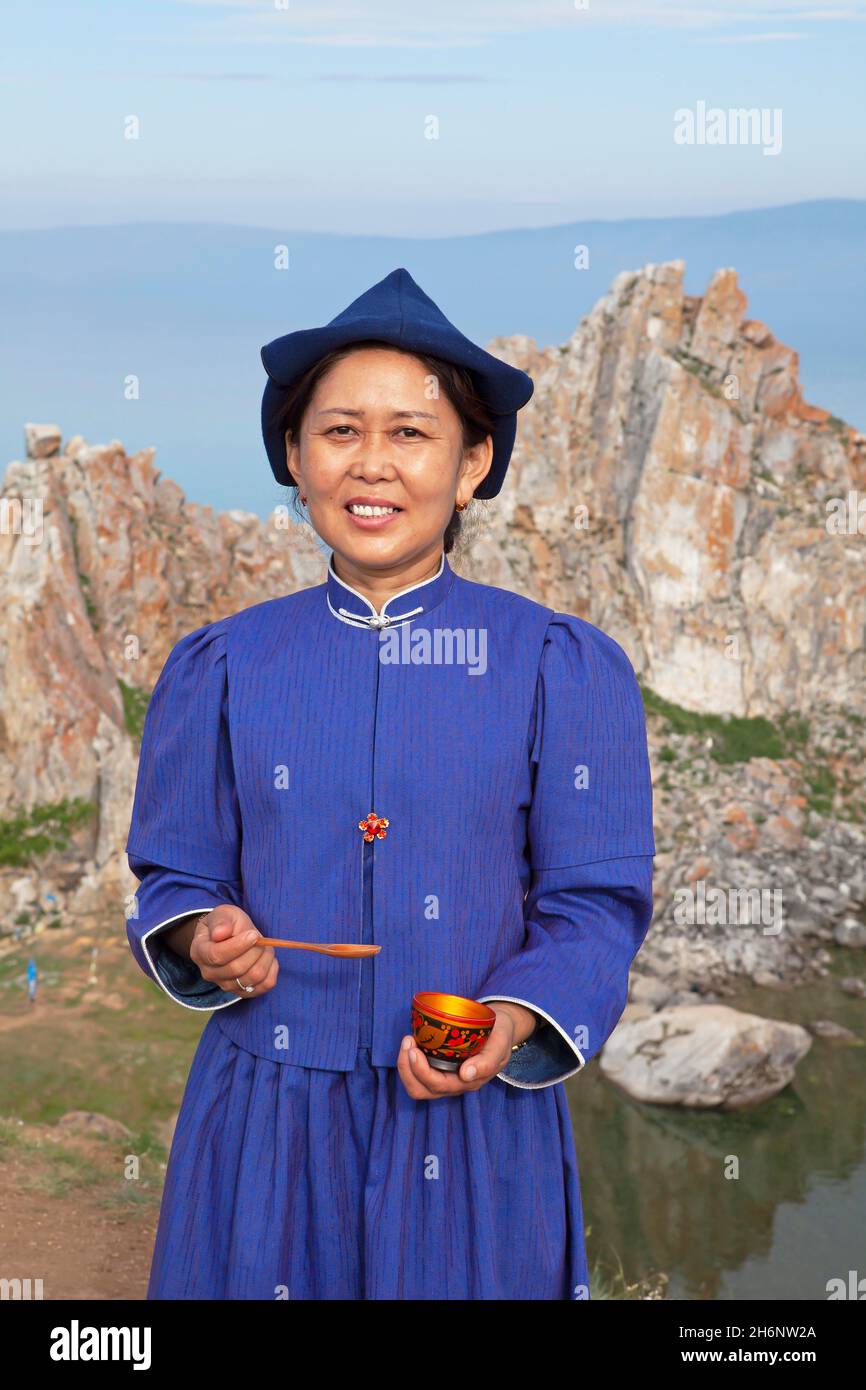 Frau, 41 Jahre, in traditioneller Tracht mit Opferschale, hinten der Schamanenfelsen, Khuzhir, Olchon Island, Pribaikalsky Stockfoto