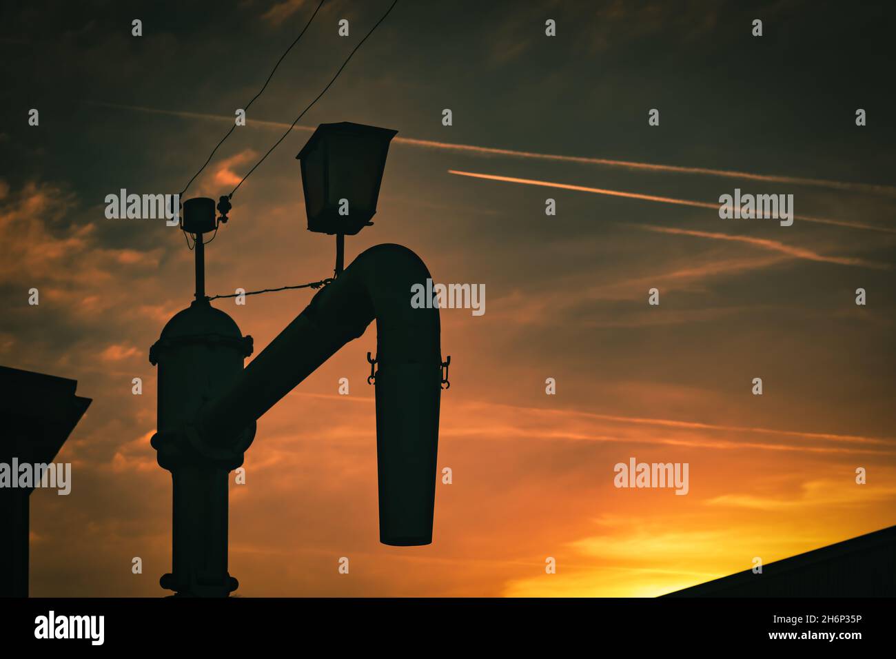 Alter Wasserkran für Dampflokomotiven vor einem roten Abendhimmel. Schönes industrielles Szenario bei Sonnenuntergang. Stockfoto