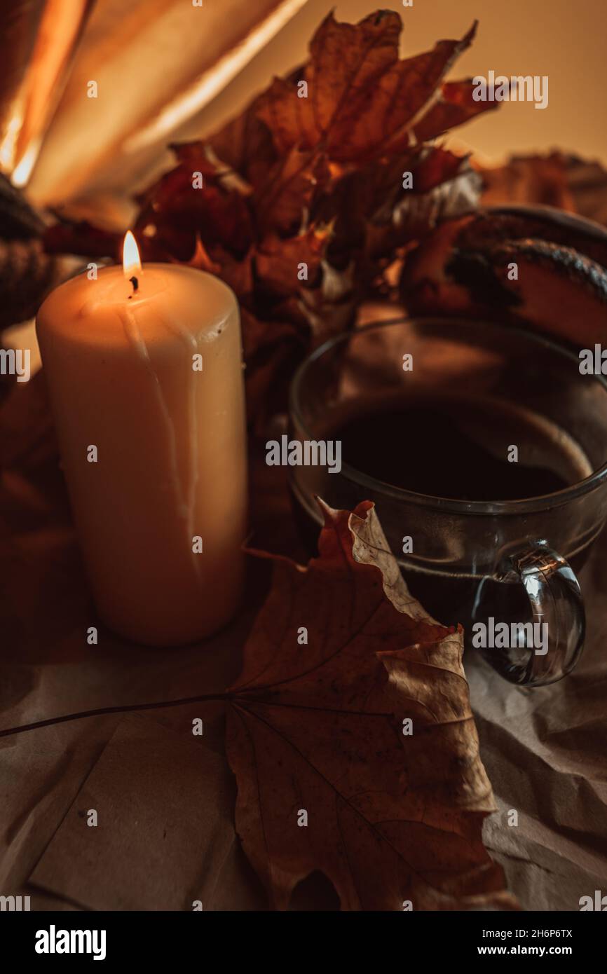 Brennende Kerze und eine große Tasse heißen schwarzen Kaffee in einem gemütlichen herbstlichen Stillleben mit trockenen Blättern. Stockfoto