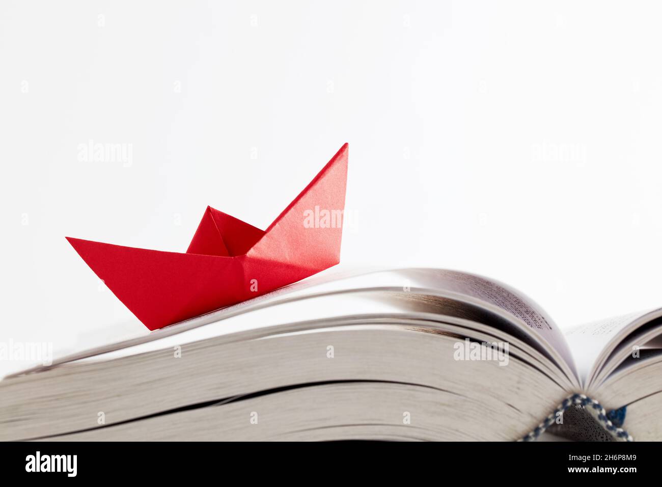 Origami rotes Papierboot schwimmt auf den Seiten eines Buches auf weißem Hintergrund. Lernen, Bildung, Lesen, Wissen oder Überwindung von Widrigkeiten Konzept. Stockfoto