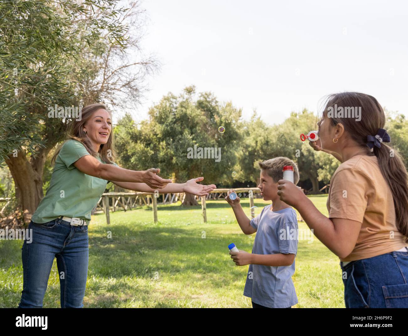 Mutter, Sohn und Tochter blasen Seifenblasen im Freien. Happychildren und Frauen mittleren Alters haben Spaß in einem Park im Sommer. Familie und Kinder outdoo Stockfoto