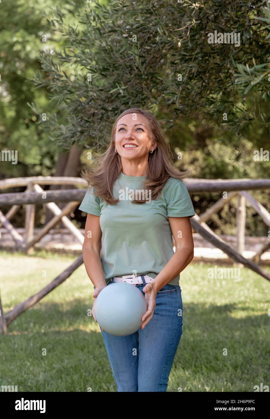 Kaukasische Frauen mittleren Alters, die T-Shirt und Jeans tragen, spielen im Park mit einem Ball, drei Viertel Schuss Stockfoto
