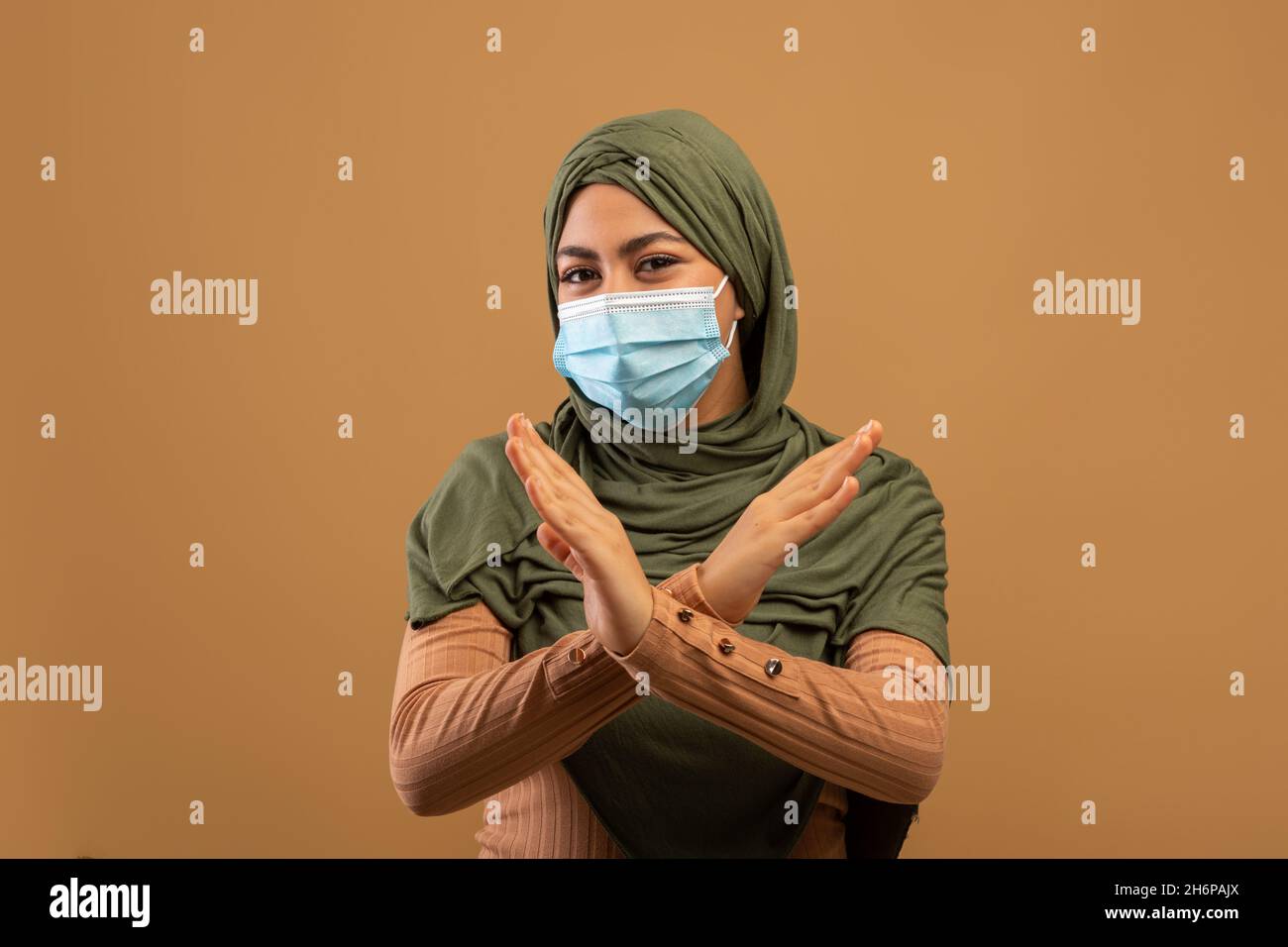 Junge muslimische Dame in Hijab trägt medizinische Gesichtsmaske, gestikulierend mit Händen, protestierend auf braunem Hintergrund Stockfoto