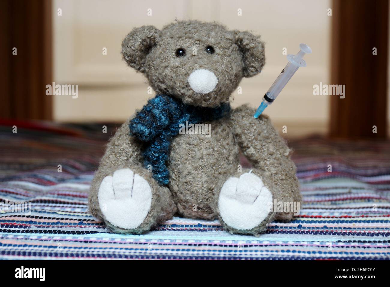 Kuscheltier Teddy mit Spritze im Arm, sitzend auf einem bunten Teppich. Stockfoto