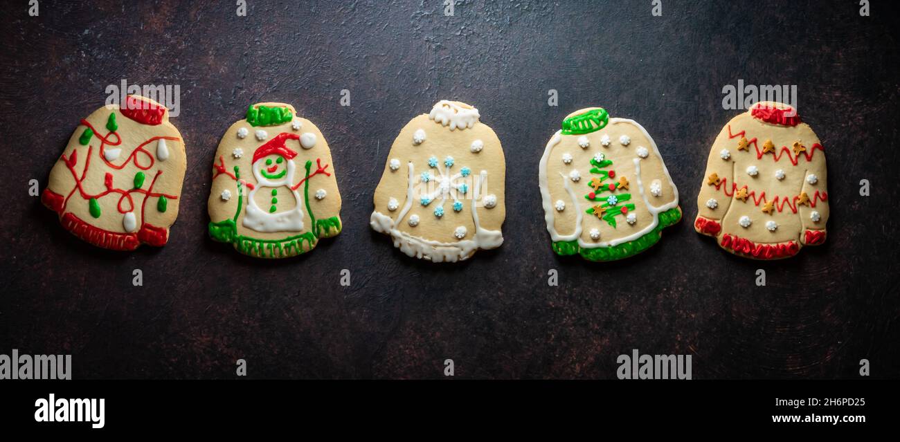 Eine Reihe hässlicher Weihnachts-Pullover-Kekse vor dunklem Hintergrund. Stockfoto