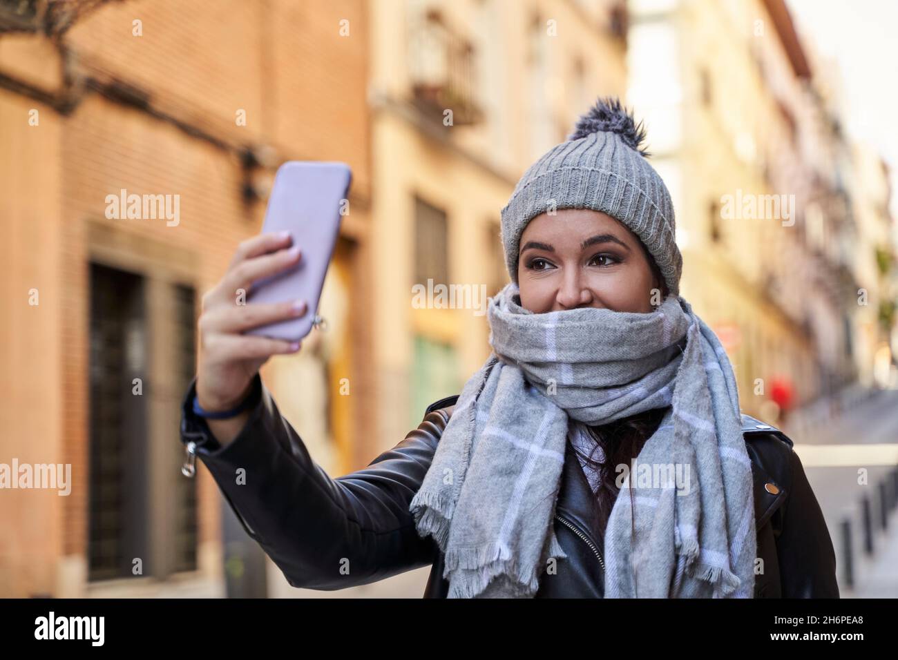 Junge Frau mit warmem Hut und Schal, die Selfie über das Smartphone am kalten Tag auf der Straße der Stadt Stockfoto