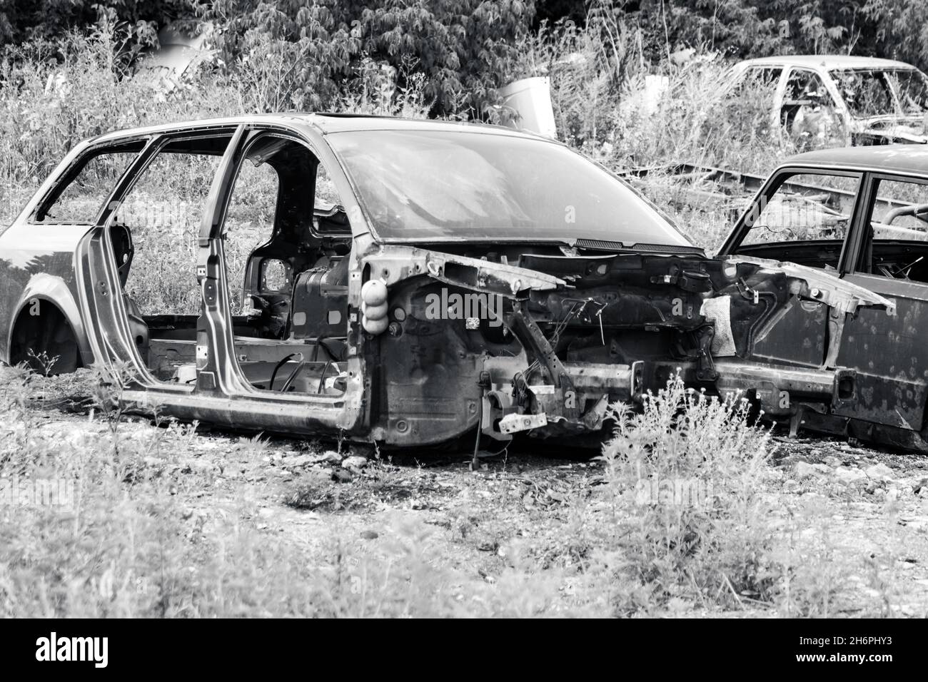 Verrostete Metallkarossenteile in Graustufen aufgegeben. Autodumpe, Wrack auf einem Schrottplatz, bereit zum Recycling Stockfoto