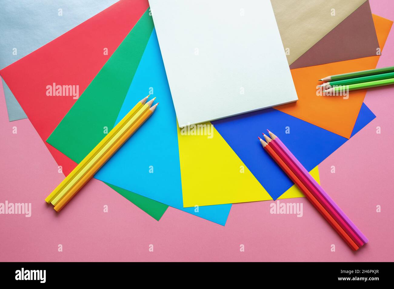 Schule und Hobby Konzepte. Bunt gefärbte Papierblätter, Buntstifte und offenes Skizzenbuch auf rosa Papierhintergrund. Freier Speicherplatz für Text oder Bild Stockfoto
