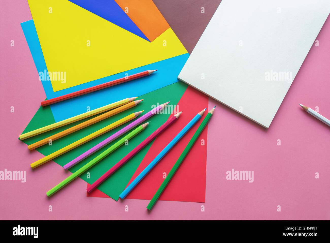 Schule und Hobby Konzepte. Farbige Papierbögen, Buntstifte und offenes Skizzenbuch auf rosa Papierhintergrund. Speicherplatz kopieren Stockfoto