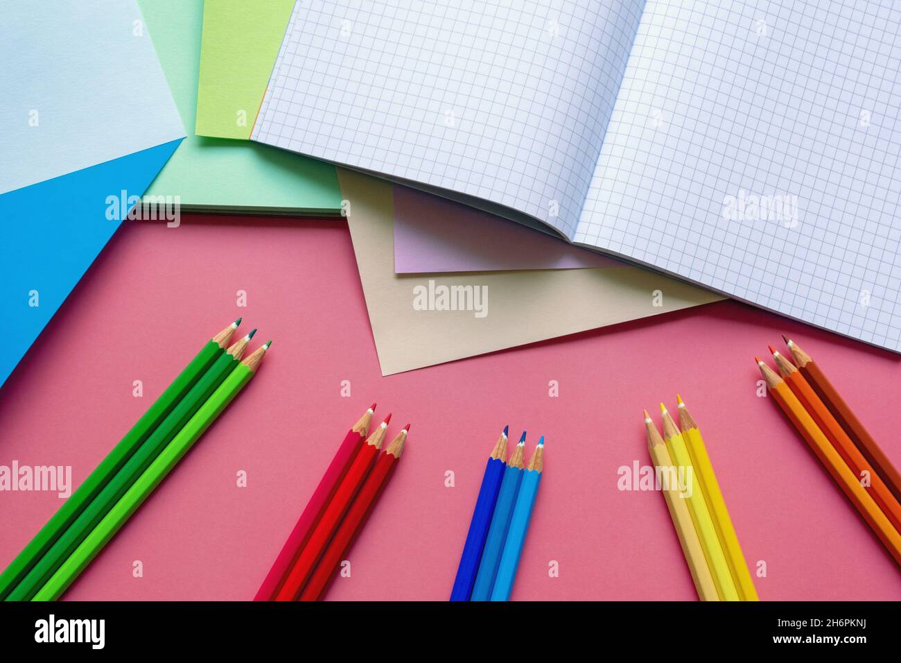 Schule und Hobby Konzepte. Farbige Papierblätter, Buntstifte und Notizbuch auf rosa Papierhintergrund. Freier Speicherplatz für Text Stockfoto