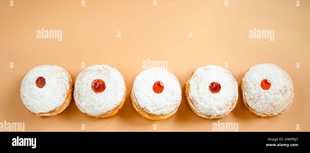 Frohes Chanukka. Traditionelles jüdisches Dessert Sufganiyot. Wir feiern den Judaismus. Donuts mit Marmelade und Zuckerpulver auf beigem Hintergrund. Bannerform Stockfoto