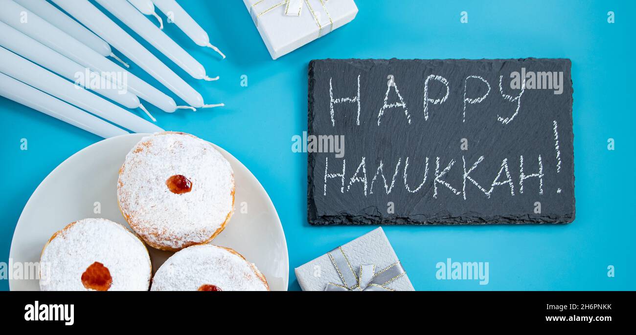 Frohes Chanukka. Jüdische Dessert sufganiyot Donuts auf blauem Hintergrund. Symbol des religiösen Judentums Feiertag. Beschriftung auf der Kreidetafel. Stockfoto