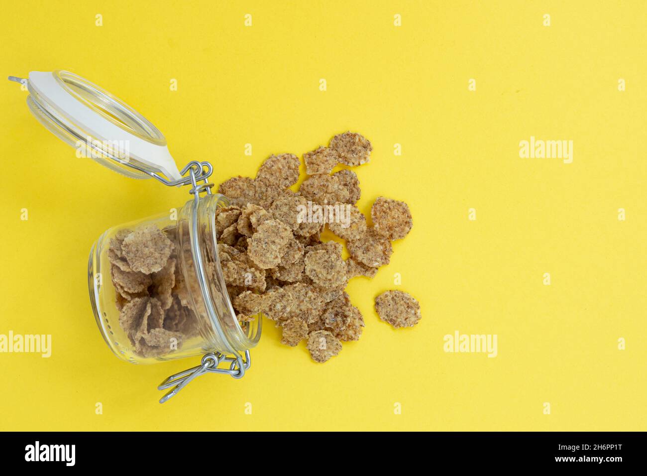 Glas mit offenem Deckel liegt auf gelbem Hintergrund, Vollkornflocken für gesundes Frühstück fallen aus ihm, leerer Platz für Text Stockfoto