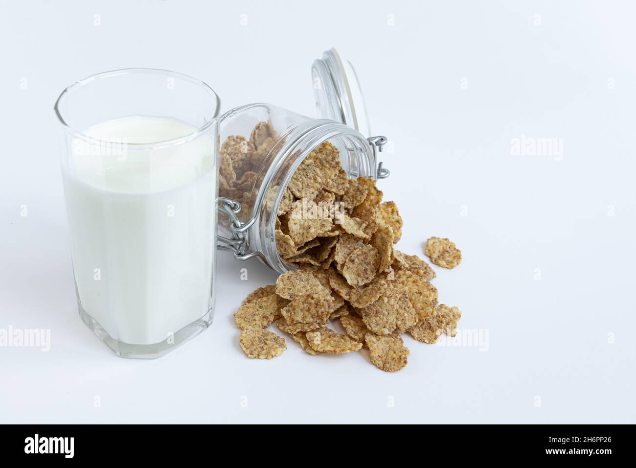 Glas mit offenem Deckel liegt auf weißem Hintergrund, Vollkornflocken für gesundes Frühstück fallen aus, transparentes Glas mit frischer Bio-Milch A Stockfoto