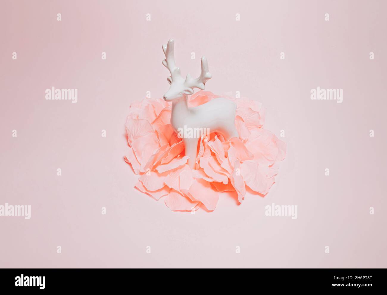 Moderne, minimalistische Winterkomposition mit pastellrosa Rosenblättern und weißem Rentier-Ornament. Minimales Weihnachtskonzept. Stockfoto
