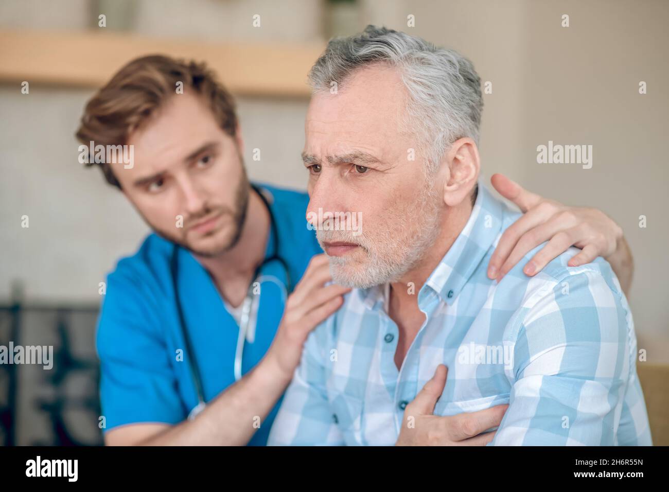 Aufmerksamer Kardiologe, der einen verängstigten kranken Mann unterstützt Stockfoto