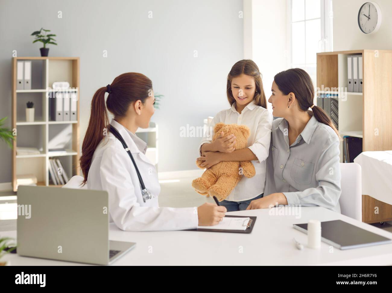 Glückliche Mutter und kleine Tochter im Gespräch mit ihrem Hausarzt in der Klinik Stockfoto