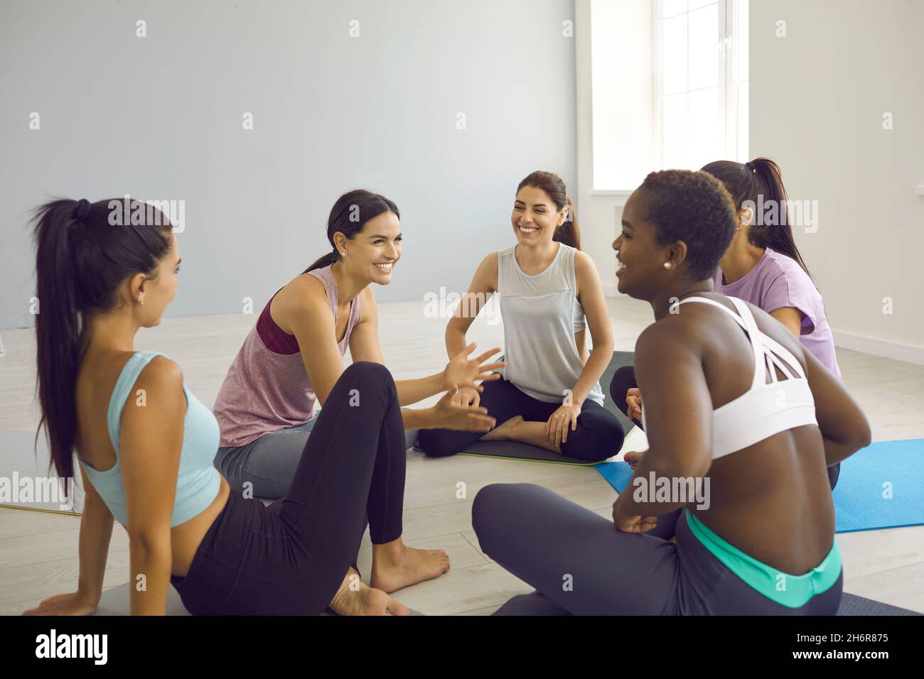 Gruppe von fröhlichen jungen athletischen multirassischen Frauen, die während der Pause im Yoga-Studio kommunizieren. Stockfoto