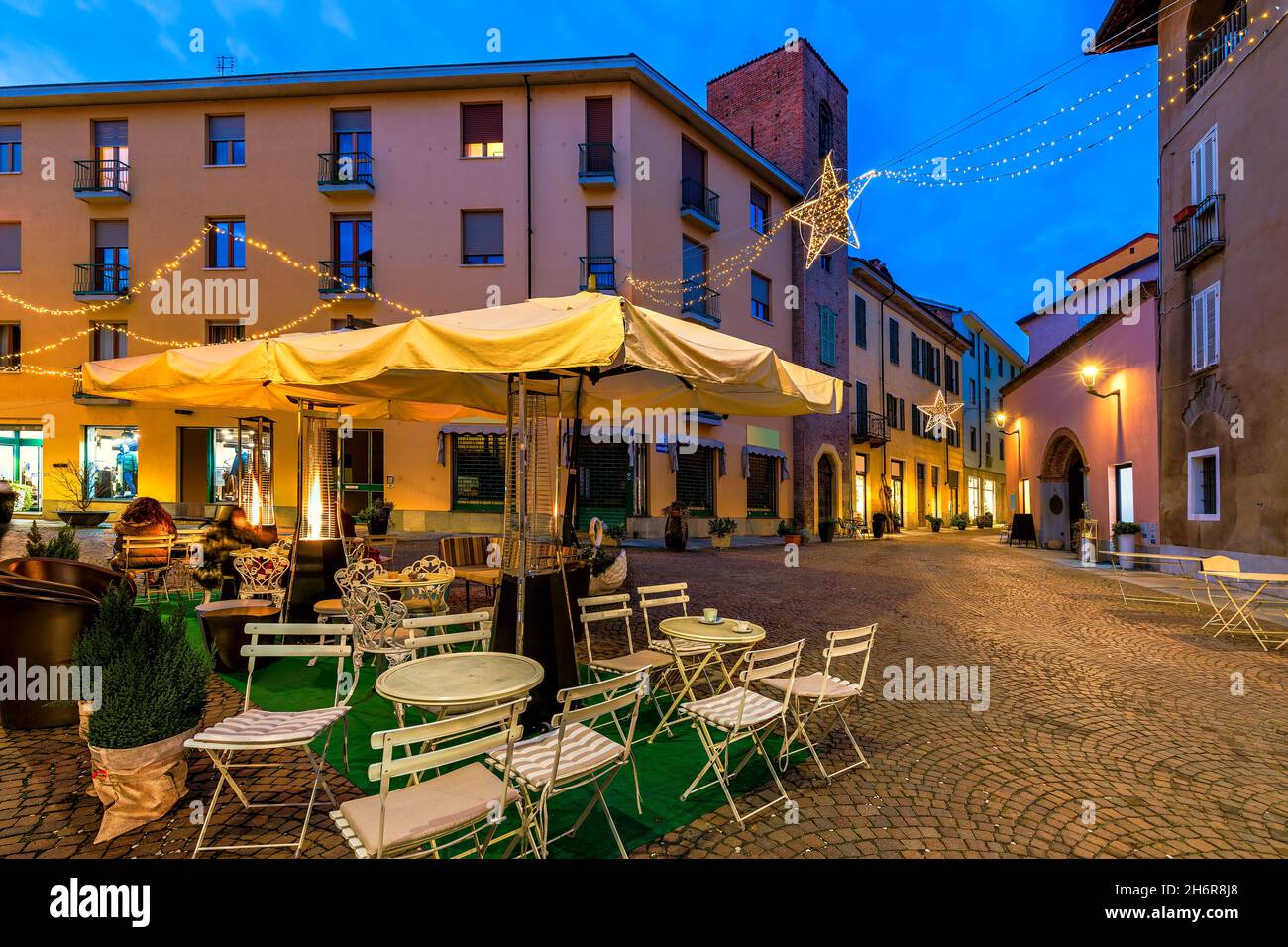 Restaurant im Freien auf einem kleinen gepflasterten Platz, der abends von Weihnachtslichtern in der Altstadt von Alba, Piemont, Norditalien, beleuchtet wird. Stockfoto