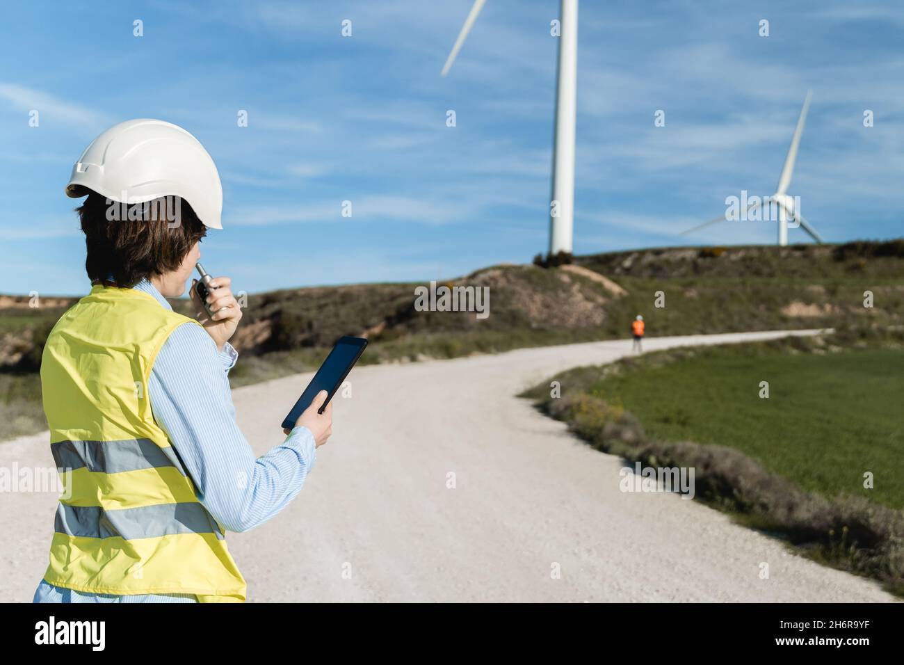 Menschen, die in einem grünen alternativen Energiepark mit Windturbinengeneratoren im Hintergrund arbeiten - Fokus auf Frau zurück Stockfoto