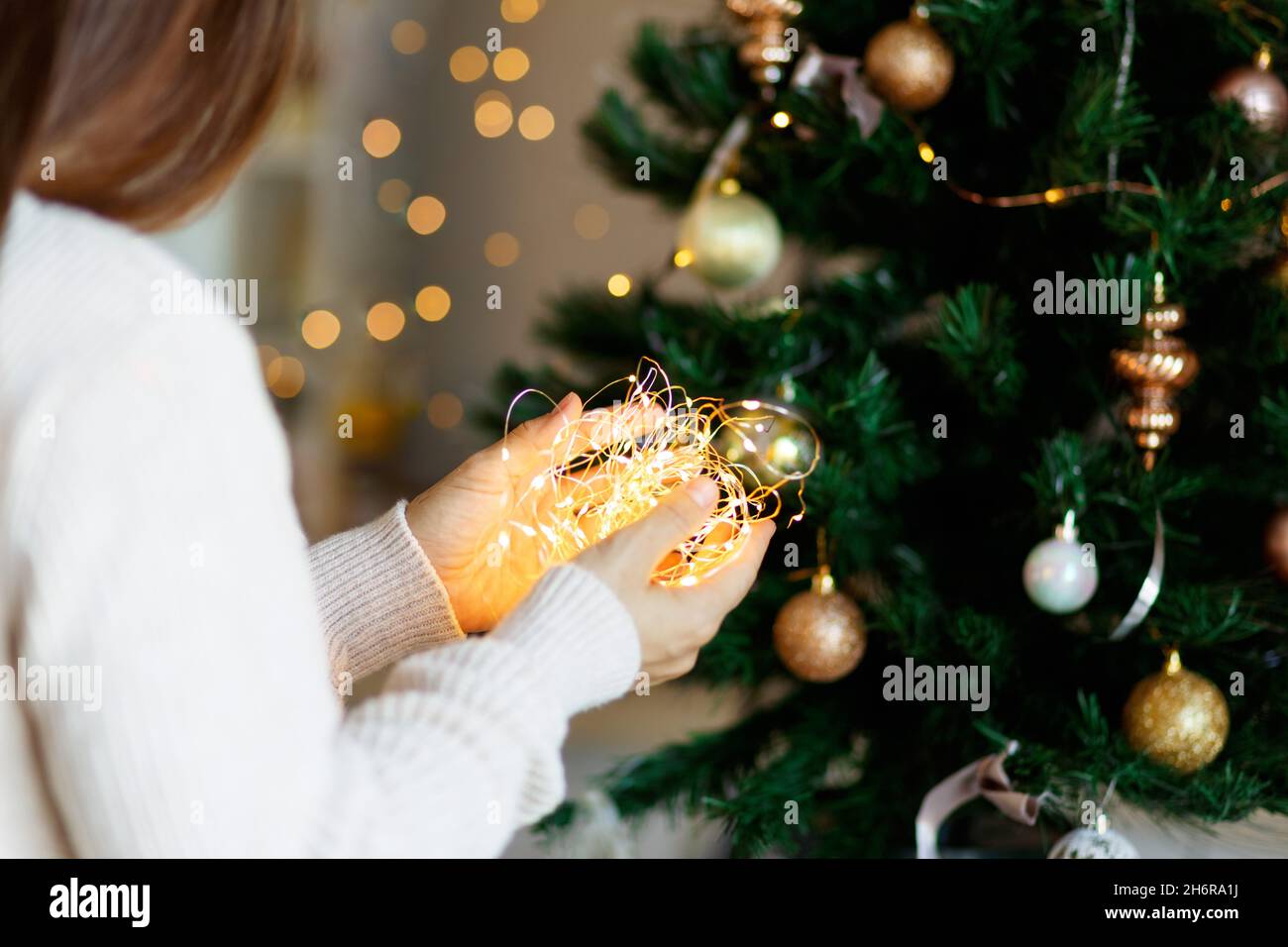 Weihnachtswunder - Frau in weißem Pullover hält glühenden LED-Licht Girlande in den Händen, Bokeh Hintergrund. Stockfoto