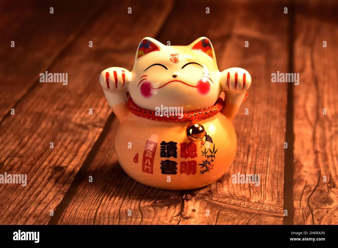 Eine japanische Glückskatze (Maneki neko) aus Porzellan auf einem rustikalen Holztisch. Stockfoto