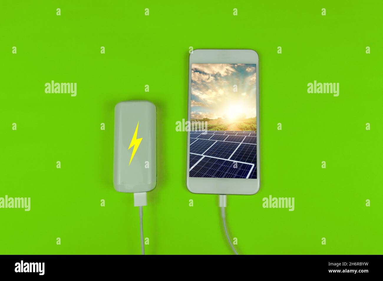 Bild Des Kreativen Konzepts „Solarbatterie“. Solarbetriebenes Mobiltelefon an eine Batterie auf grünem Hintergrund angeschlossen. Stockfoto