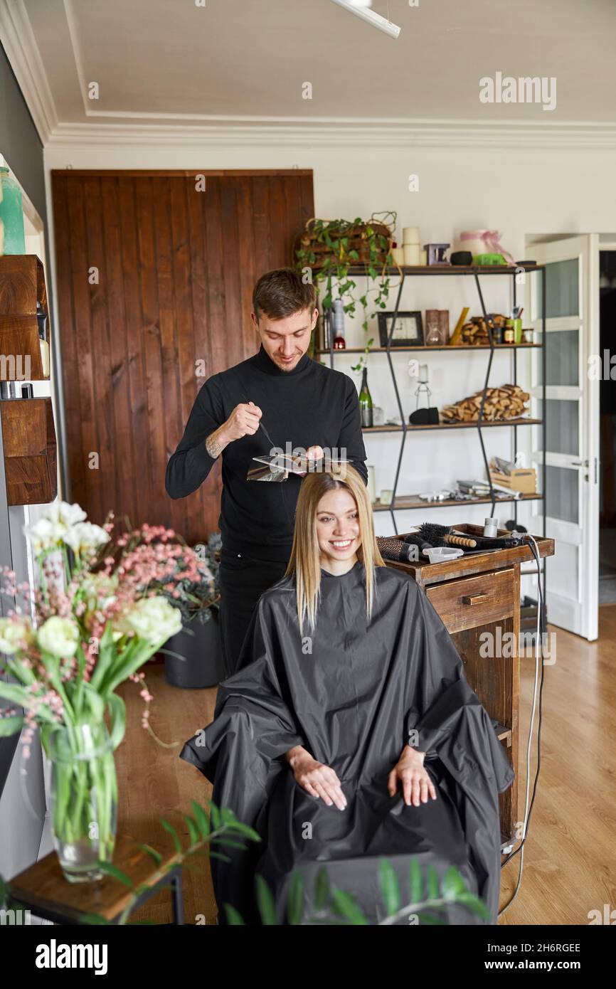 Selbstbewusster männlicher Stylistin färben die Haare des blonden kaukasischen weiblichen Kunden Stockfoto