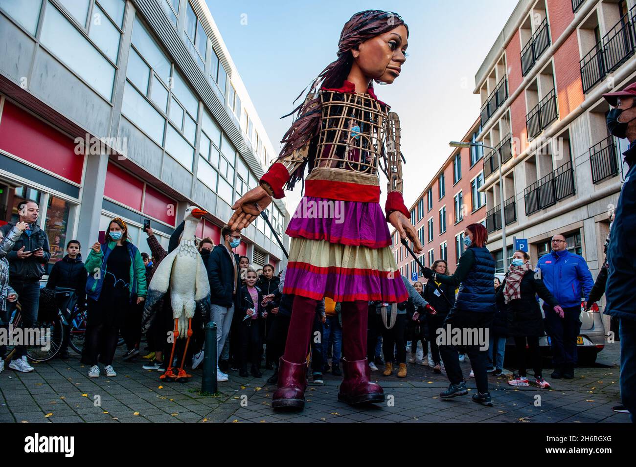 Der kleine Amal wird von einem Marionettenstorch begleitet und beginnt vor dem Theater zu laufen.Amare, ein neues kulturelles Zentrum im Zentrum von Den Haag, hat im Rahmen seines "Offenen Festivals" den Besuch der riesigen Marionette "kleiner Amal" organisiert, Ein neun Jahre altes Mädchen aus Syrien, das über 11 Meter groß ist, um das Theater „De Vaillant“ zu besuchen, das für seine kulturelle Vielfalt bekannt ist und das Ziel verfolgt, die kulturelle Beteiligung aller Bewohner von Den Haag zu erhöhen. Von dort aus spazierte der kleine Amal, begleitet von Kindern, durch die Nachbarschaft und spielte dort. Stockfoto