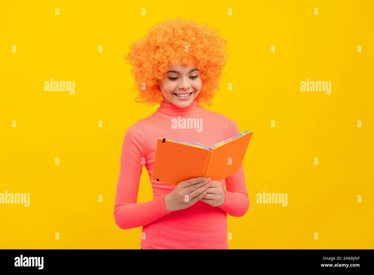 Glückliches Mädchen Kind mit orangen Haaren in rosa Poloneck Lächeln Lesen Schulbuch, Wissen Stockfoto