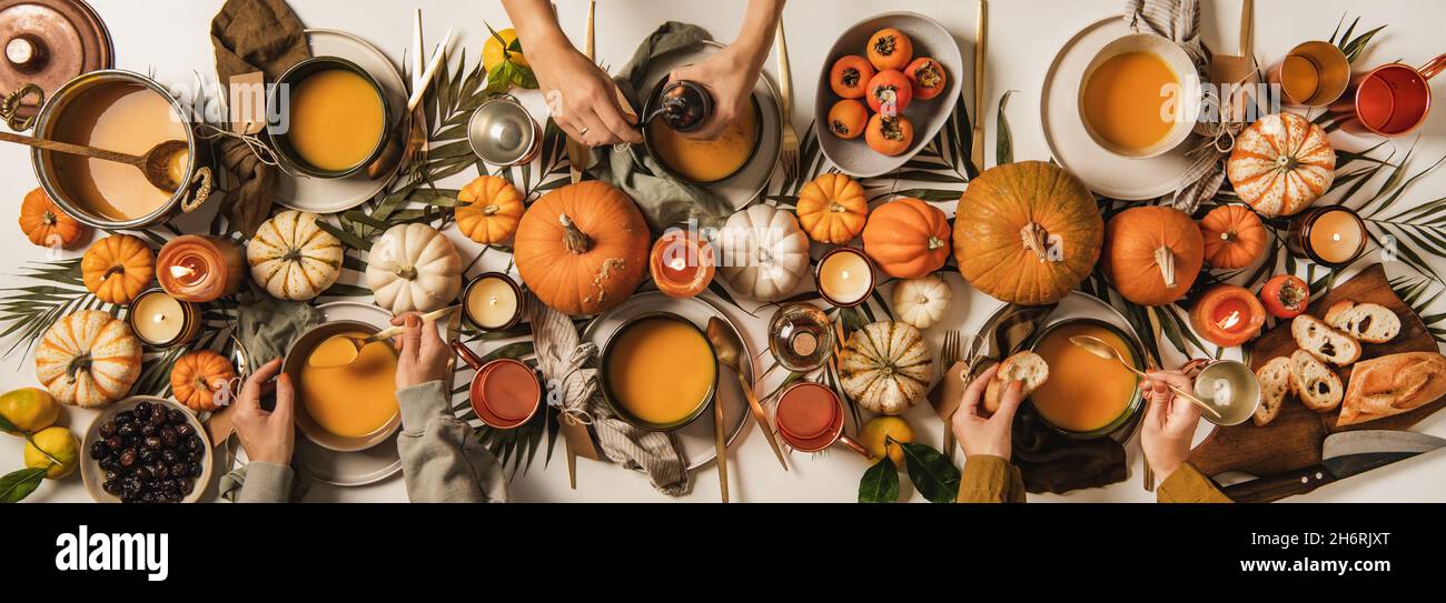 Hände von Menschen, die Kürbissuppe über einem dekorierten Tisch essen Stockfoto