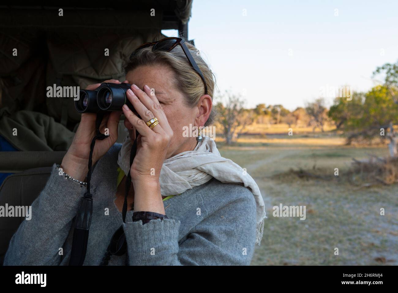 Erwachsene Frau schaut durch ein Fernglas und steht neben einem Jeep. Stockfoto