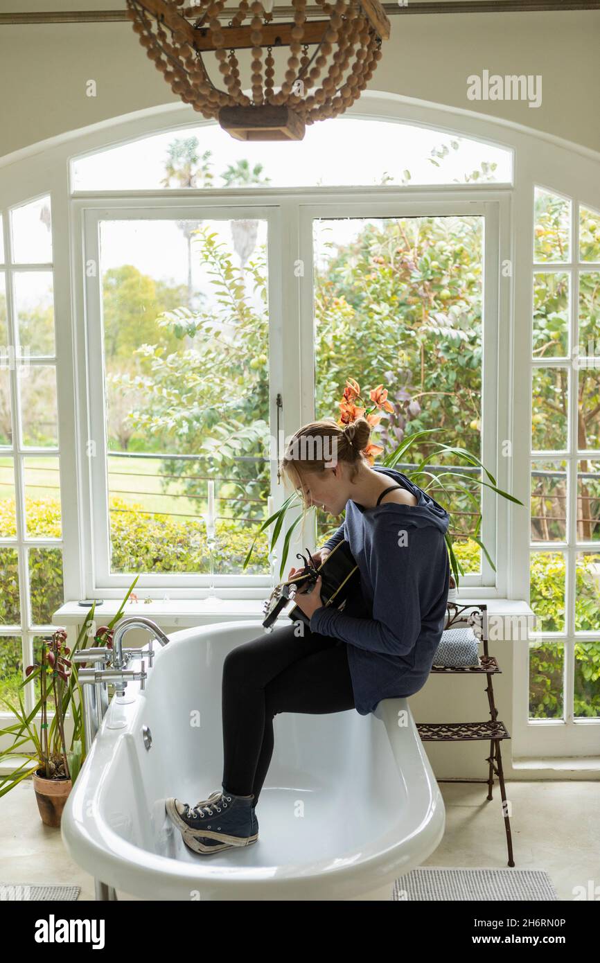 Teenager-Mädchen, das am Rand einer Badewanne sitzt und Gitarre spielt und singt. Stockfoto