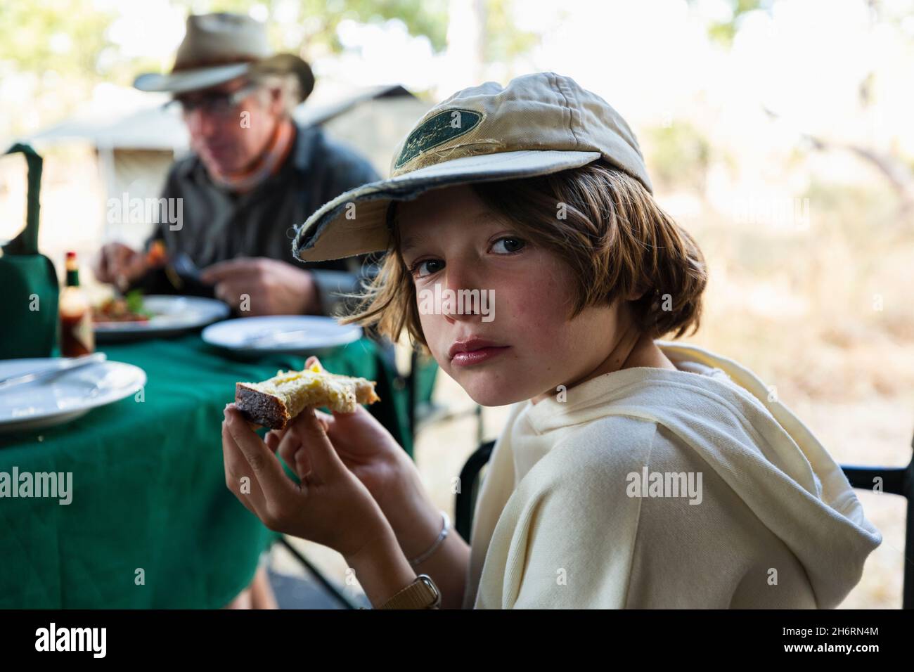 Kleiner Junge, der ein Stück Toast an einem Tisch in einem Safari-Camp isst Stockfoto