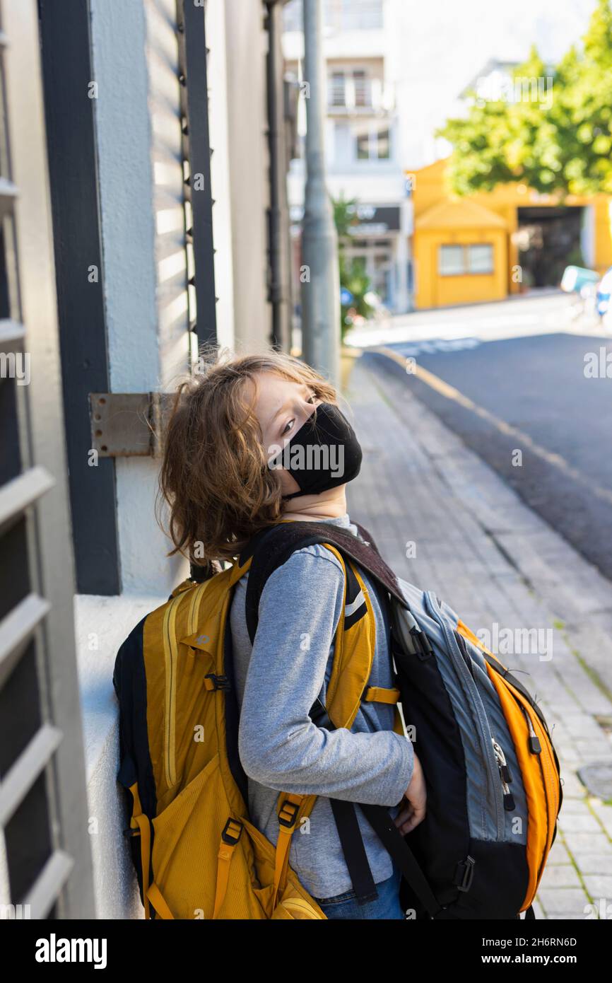Ein Junge, der einen Rucksack mit einem schwarzen Gesichtsbeet auf einer Straße trägt. Stockfoto