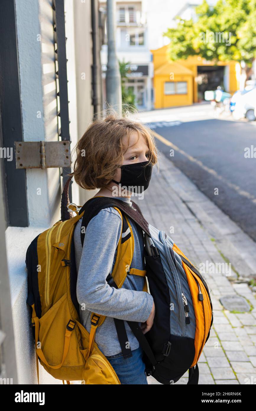Ein Junge, der einen Rucksack mit einem schwarzen Gesichtsbeet auf einer Straße trägt. Stockfoto