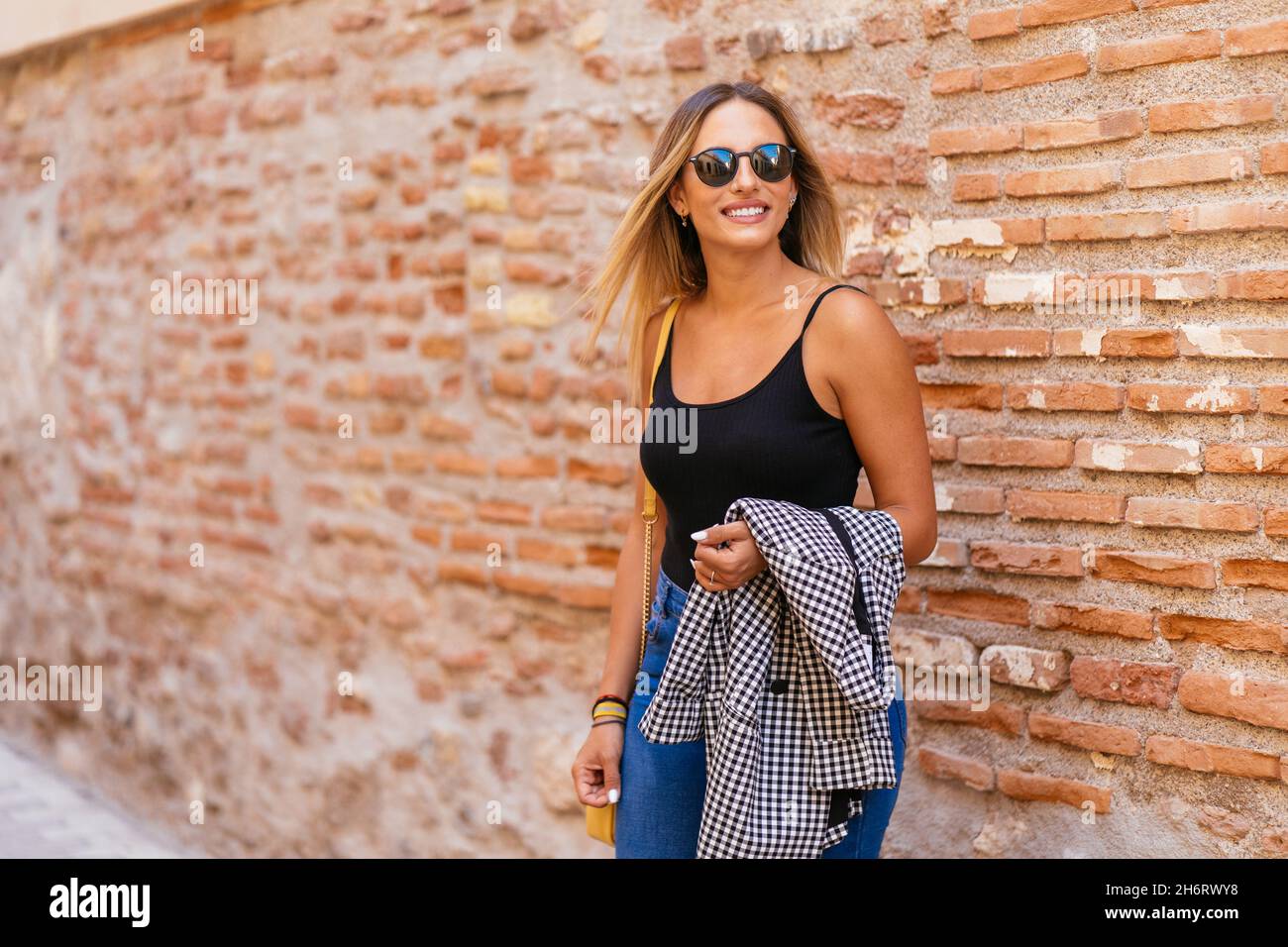 Stilvolle Frau, die in der Nähe einer Backsteinmauer in der Stadt steht Stockfoto