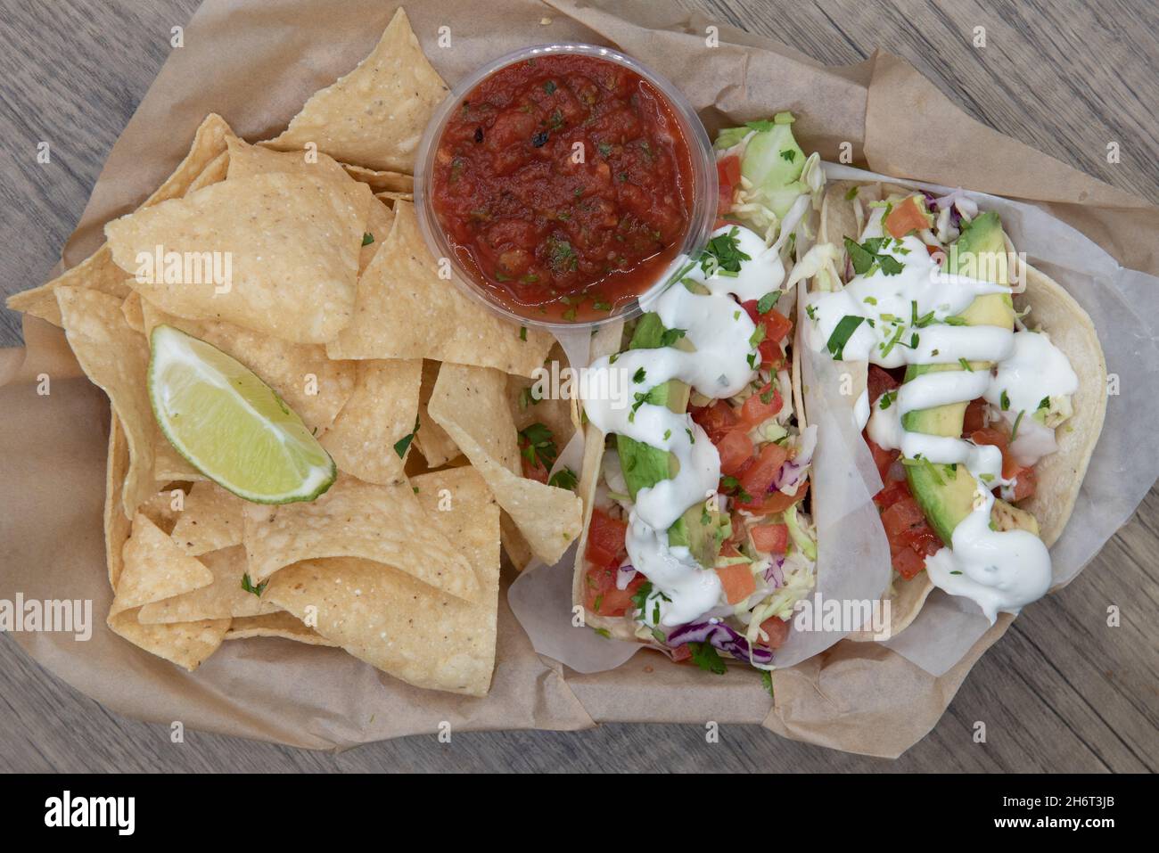 Blick von oben auf einen herzhaften Korb voller Chips und Salsa zum Essen mit drei Fischtacos. Stockfoto